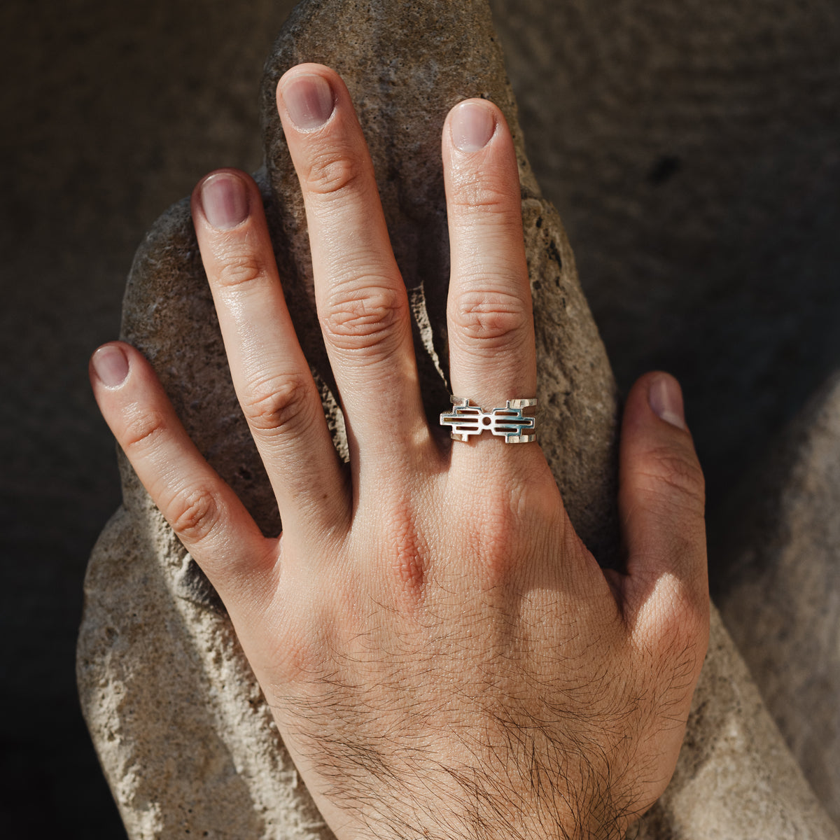 Bague homme double-face en argent 925 hsquare1 murumio portée à l'index d'une main sur une pierre